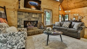 A cabin with a stone fireplace, a television mounted above it, a sofa, and a coffee table. - Happy Hideaway | Mineral Bluff, Ga (Mineral Bluff)