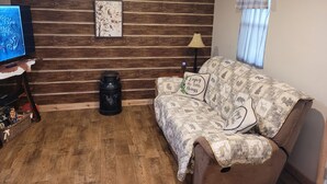 Una sala de estar acogedora con una pared de madera, un sofá con cojines estampados, un televisor y una lámpara.