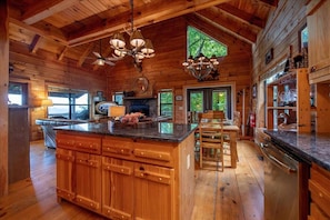 Un interior de cabaña espacioso con una gran mesa de comedor de madera, una cocina empotrada con encimeras de granito y una chimenea.