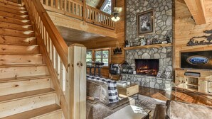 Ein Interieur einer Holzhütte mit Kamin aus Stein, einer Holztreppe und einem Fernseher auf einem Holzkasten.