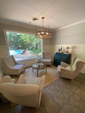 Relax in a spacious living room with a sofa, armchairs, and a coffee table, offering a view of the pool and lush greenery.