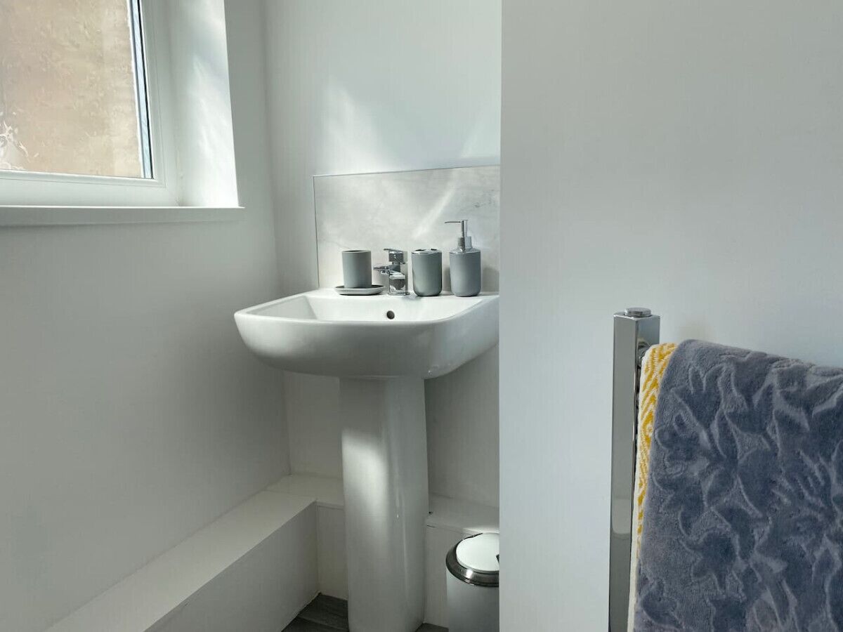 A bathroom with a white pedestal sink, a toilet, and a towel rack with a patterned towel.