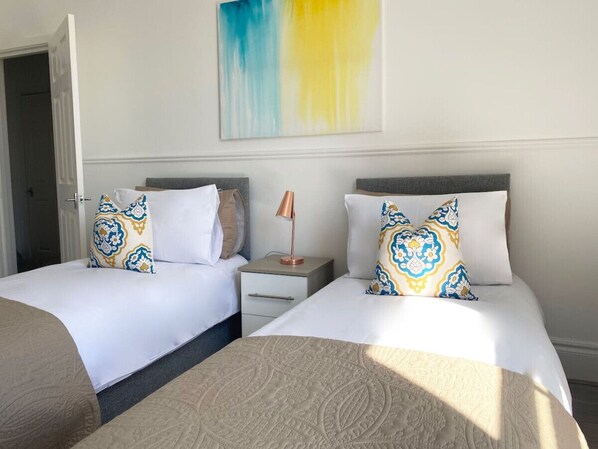 A hotel room with two beds, a nightstand, a lamp, and a large abstract painting on the wall.
