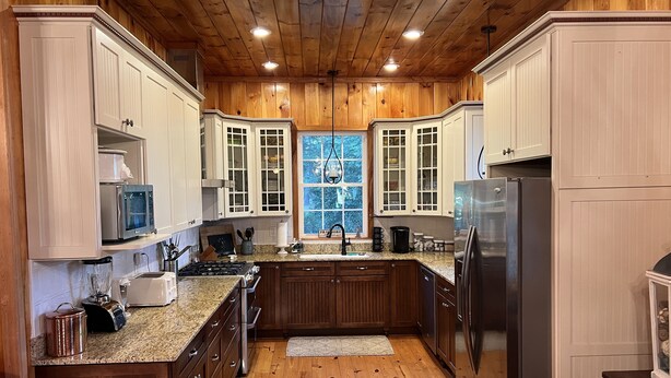 A kitchen with wooden cabinets, a granite countertop, a stainless steel refrigerator, and a window with a view of trees. - Creekside Country Cottage- minutes away from I-95 (Manning)