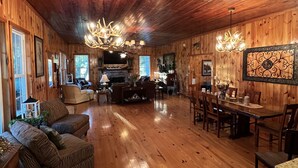 A spacious room with wooden floors, a fireplace, a dining area, and a chandelier. - Creekside Country Cottage- minutes away from I-95 (Manning)