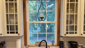 A kitchen with wooden cabinets, a granite countertop, a window with a view of greenery, a black faucet, and a coffee station. - Creekside Country Cottage- minutes away from I-95 (Manning)