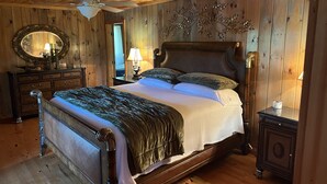 A wooden-paneled bedroom with a large bed, a ceiling fan, a mirror, and a dresser. - Creekside Country Cottage- minutes away from I-95 (Manning)