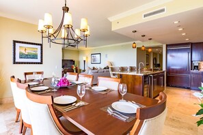 Un comedor con una mesa de madera dispuesta para seis personas, rodeada de sillas. Un candelabro cuelga sobre la mesa.