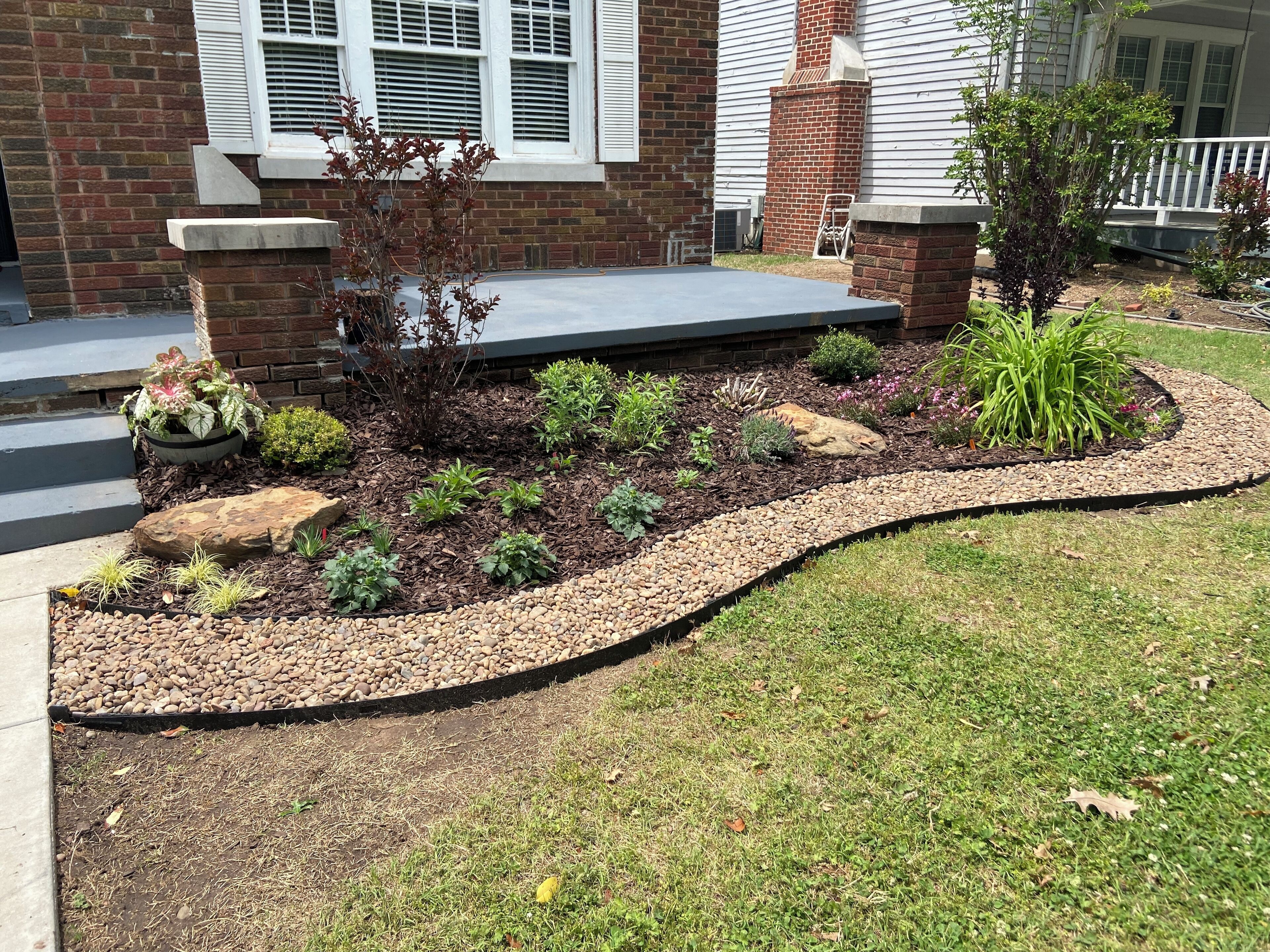 A landscaped garden with a variety of plants and a curved stone pathway.