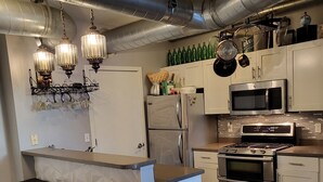 Eine moderne Küche mit Edelstahlgeräten, einer zentralen Kochinsel mit Barhocker und freiliegenden Lüftungsrohren an der Decke.