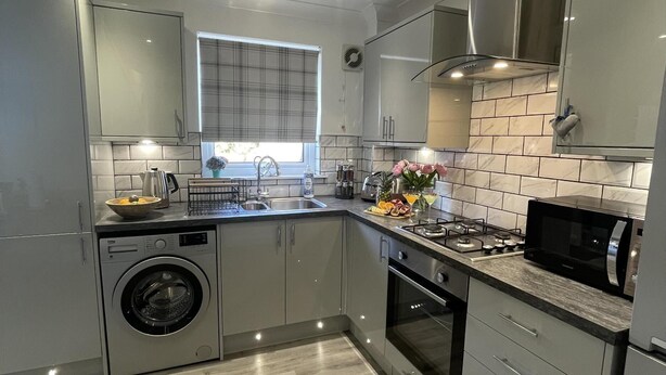 A modern kitchen with a built-in washing machine, stainless steel appliances, and a window with blinds. - 2 Bed House - Sleeps 4 - Garden, Parking, Wifi (Perth)