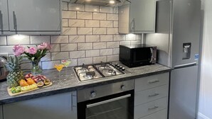 A modern kitchen with a gas stove, microwave, refrigerator, and marble backsplash. - 2 Bed House - Sleeps 4 - Garden, Parking, Wifi (Perth)