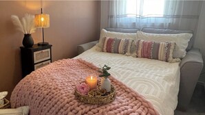 A neatly made bed with a pink blanket, a lit candle, and decorative pillows. - 2 Bed House - Sleeps 4 - Garden, Parking, Wifi (Perth)