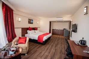 Ein Hotelzimmer mit Bett, Schreibtisch, Stuhl, einem kleinen Tisch mit Weingläsern und einer Küchenzeile.
