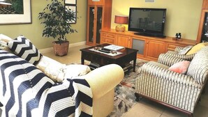 A living room with a sofa, armchair, coffee table, television, cabinet, and a potted plant. - Your Home Away From Home in a Charming Street (West Launceston)