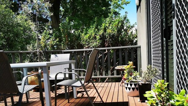 A wooden deck with a table and chairs, surrounded by potted plants and a lattice fence. - Your Home Away From Home in a Charming Street (West Launceston)