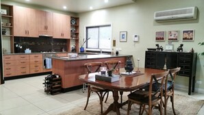 A kitchen with wooden cabinets, a central island, a dining table with chairs, and a tiled floor. - Your Home Away From Home in a Charming Street (West Launceston)