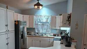 Una cocina con armarios blancos, un refrigerador, un fregadero, una estufa y una mesa de comedor con sillas.