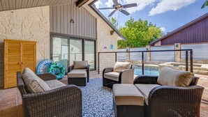 Ein überdachter Patio-Bereich mit Rattanmöbeln, einem Deckenventilator und Blick auf einen Swimmingpool.