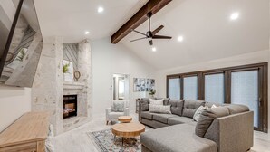 Ein modernes Wohnzimmer mit Kamin, einem großen, grauen Ecksofa, einem runden Couchtisch aus Holz und einem Deckenventilator.