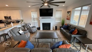 A modern living room with a fireplace, a large flat-screen TV, and a ceiling fan. - New home-3 miles to DT Flag!! With grill, firepit, AC (Flagstaff)
