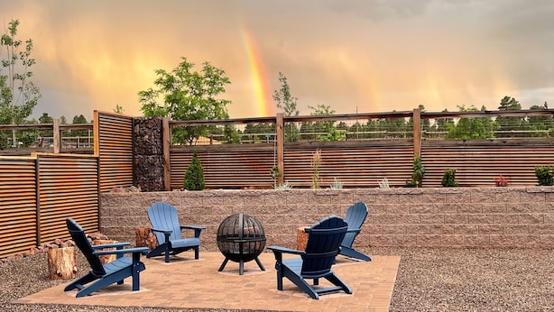 An outdoor seating area with Adirondack chairs and a fire pit, surrounded by a wooden fence and stone walls. - New home-3 miles to DT Flag!! With grill, firepit, AC (Flagstaff)