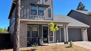 A two-story house with a stone facade, large windows, and a small front yard with a tree. - New home-3 miles to DT Flag!! With grill, firepit, AC (Flagstaff)