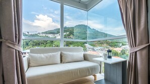 A modern room with a sofa, a small table, and a view of a green hillside. - Ozone Condo by Lofty (Karon)