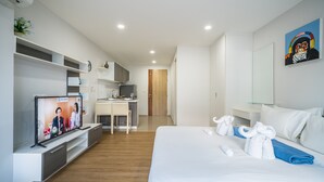 A modern hotel room with a large bed, a desk, and a television displaying a video call. - Ozone Condo by Lofty (Karon)