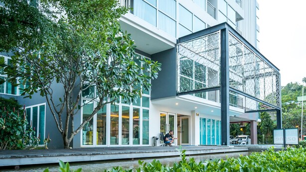 A modern building with large windows, a covered outdoor area, and a tree in the foreground. - Ozone Condo by Lofty (Karon)