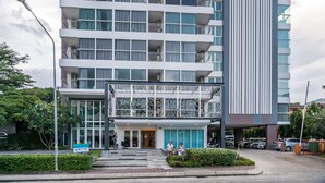 A multi-story hotel with a modern design, featuring balconies on each floor, a prominent entrance with glass doors, and a sign indicating a sale office. - Ozone Condo by Lofty (Karon)