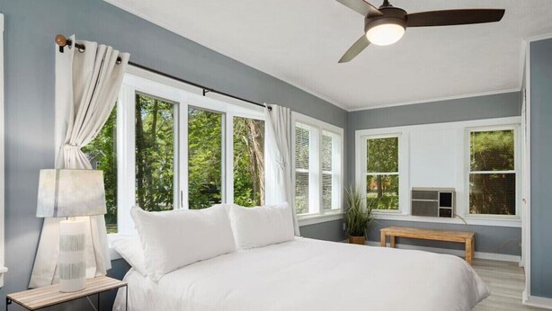 Un dormitorio con una cama grande, ventilador de techo y varias ventanas.