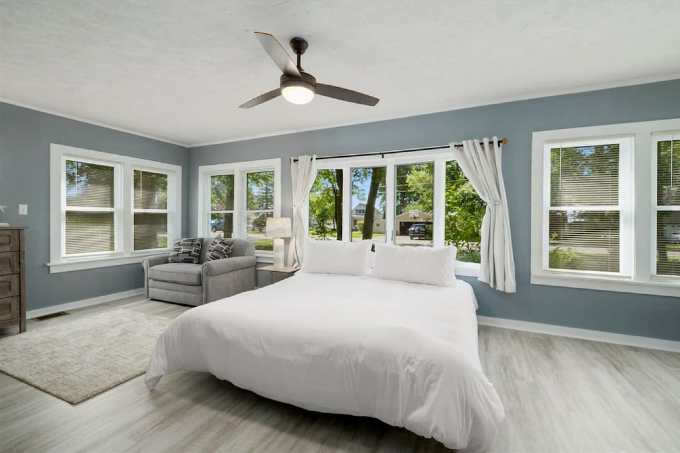 A bedroom with a large bed, a ceiling fan, and multiple windows.