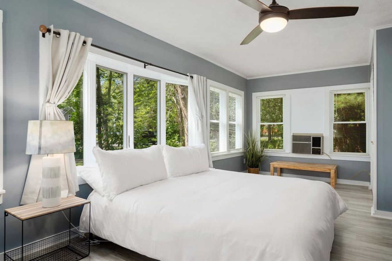 A bedroom with a large bed, a ceiling fan, and multiple windows.