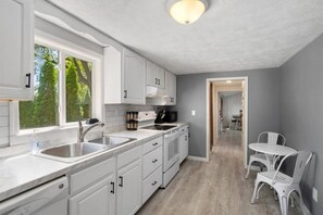 A modern kitchen with white cabinetry, a large window, and a view of trees. - The Brew Bungalow-Oneida Lakeside Getaway (Verona) (Canastota)