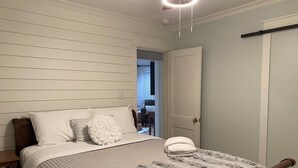 Ett sovrum med en säng, en träfärgad sänggavel, en vit dörr och en taklampa.