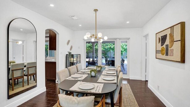 Une salle à manger avec une longue table dressée pour six personnes, un lustre et un grand miroir sur le mur de gauche.