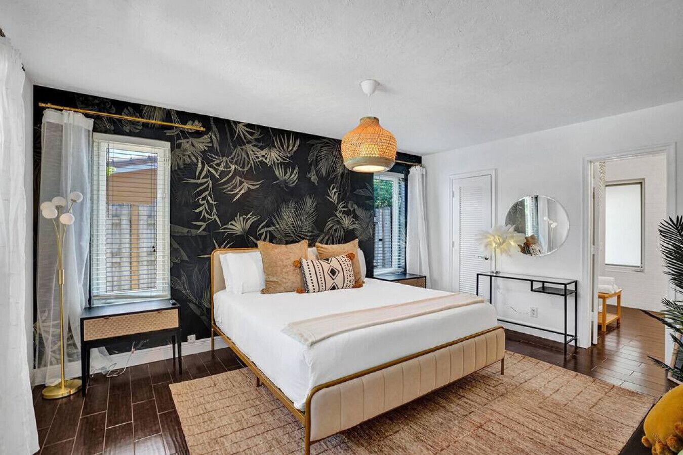 A modern bedroom with a large bed, a hanging light fixture, and a view of the outdoors through the window.