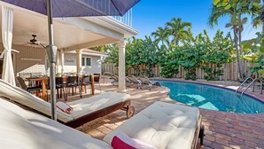 Un espace aménagé au bord de la piscine, avec des chaises longues, un patio couvert et une piscine.