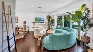 Un salon moderne avec un canapé incurvé de couleur turquoise, une échelle en bois, un téléviseur fixé au mur et de grandes fenêtres.