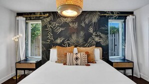 Une chambre avec un grand lit, deux tables de chevet, un luminaire suspendu et une fenêtre avec des rideaux.