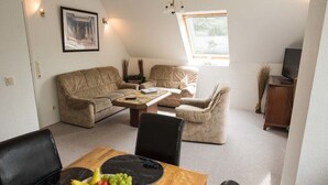 Una sala de estar acogedora con una mesa de comedor dispuesta con frutas, un sofá y un televisor.