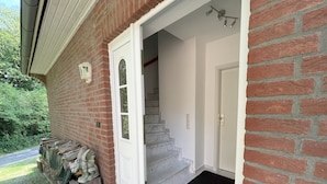 Fachada de ladrillo con una puerta blanca, una escalera de mármol y un felpudo negro en la entrada.
