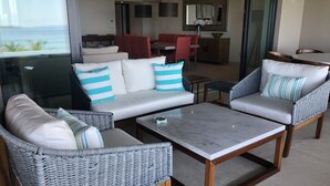 A modern living room with a sofa, two armchairs, a coffee table, and a dining area with a red table and chairs. - Condo Azul :Ocean View • Private Pool • Premier Access • Golf Cart • Housekeeper (Punta de Mita)