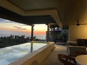 A modern outdoor seating area with a view of the ocean at sunset.