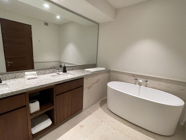 A modern bathroom with a freestanding bathtub, a large mirror, and a marble countertop.