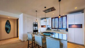 A modern kitchen with a central island, bar stools, pendant lighting, and a large window with blinds. - Condo Azul :Ocean View • Private Pool • Premier Access • Golf Cart • Housekeeper (Punta de Mita)