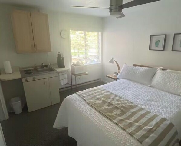 A bedroom with a bed, a desk, a window, and a ceiling fan.