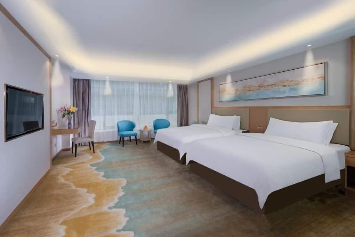 A hotel room with two beds, a desk, a chair, and a TV.