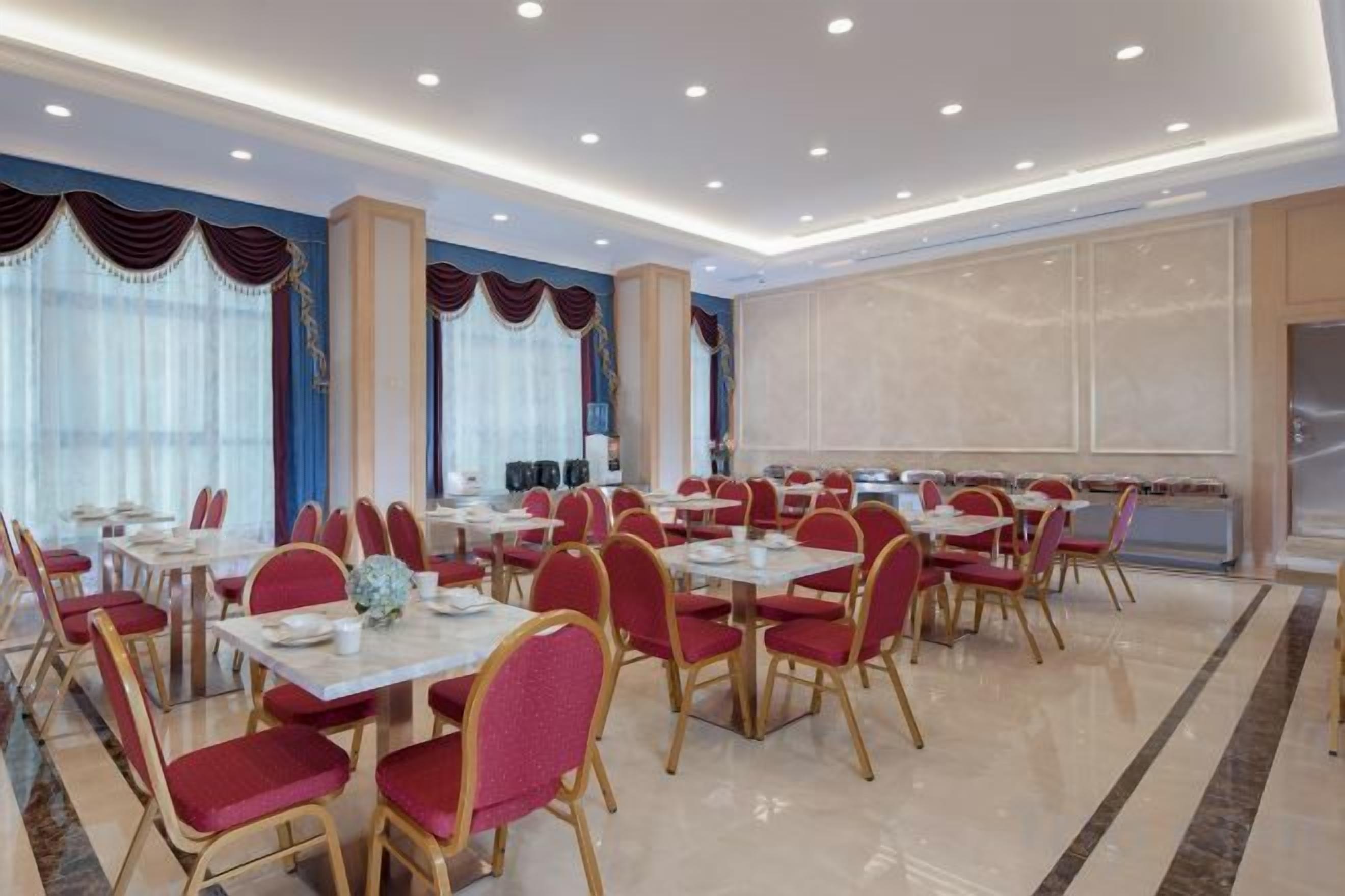 A hotel dining area with tables and chairs, a large window, and a view of the city.